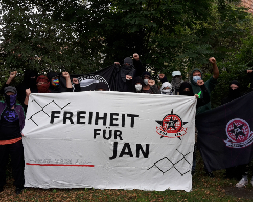 Foto mit vermummten Personen die ein Banner mit der Aufschrift Freiheit für Jan halten sowie eine Antifa Fahne und eine FdA Fahne